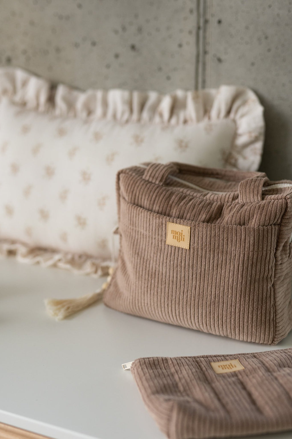 1. Latte-colored makeup bag with ribbed texture and Moi Mili logo, styled on a white surface with a decorative pillow