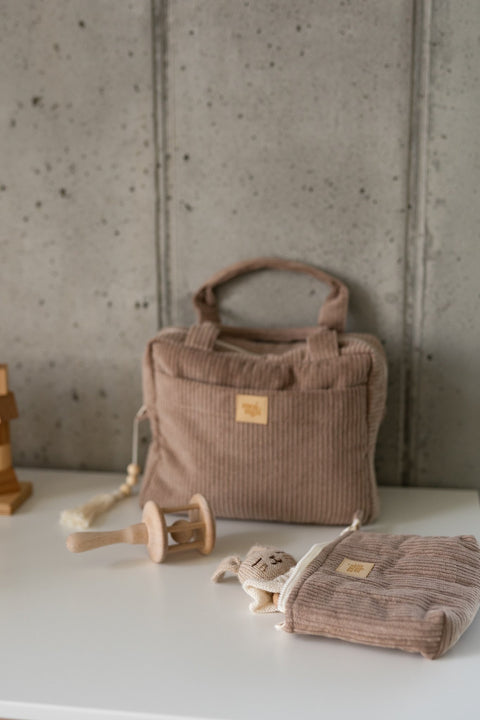 1. Latte-colored makeup bag with ribbed texture and Moi Mili logo, styled with wooden toys on a white surface