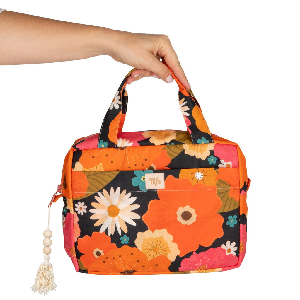 2. Hand holding orange floral makeup bag with tassel, featuring daisies and leaves, on white background