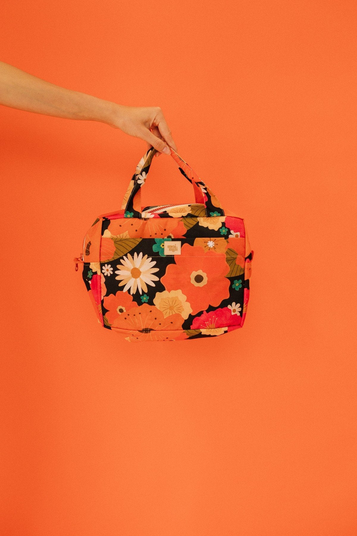 2. Woman holding orange floral makeup bag with daisies and leaves against matching orange background