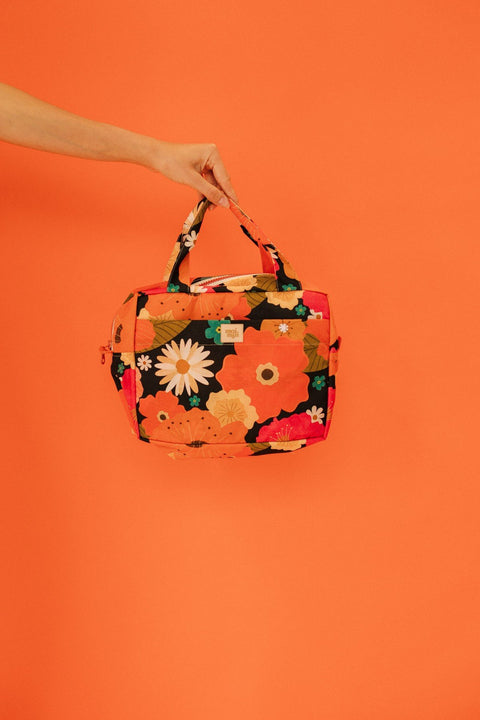 2. Woman holding orange floral makeup bag with daisies and leaves against matching orange background