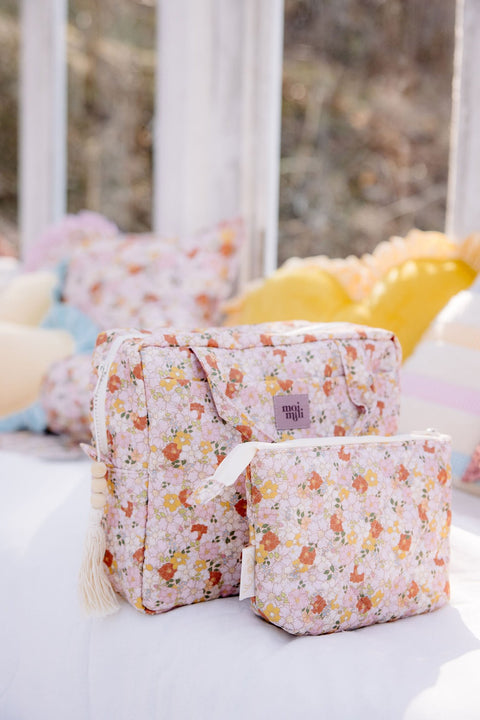 1. Floral print makeup bag set on a bed with colorful pillows in the background, showcasing large and small sizes