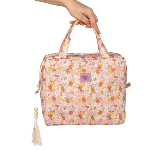 1. Hand holding Moi Mili large makeup bag with floral print and tassel, showing front logo and handles