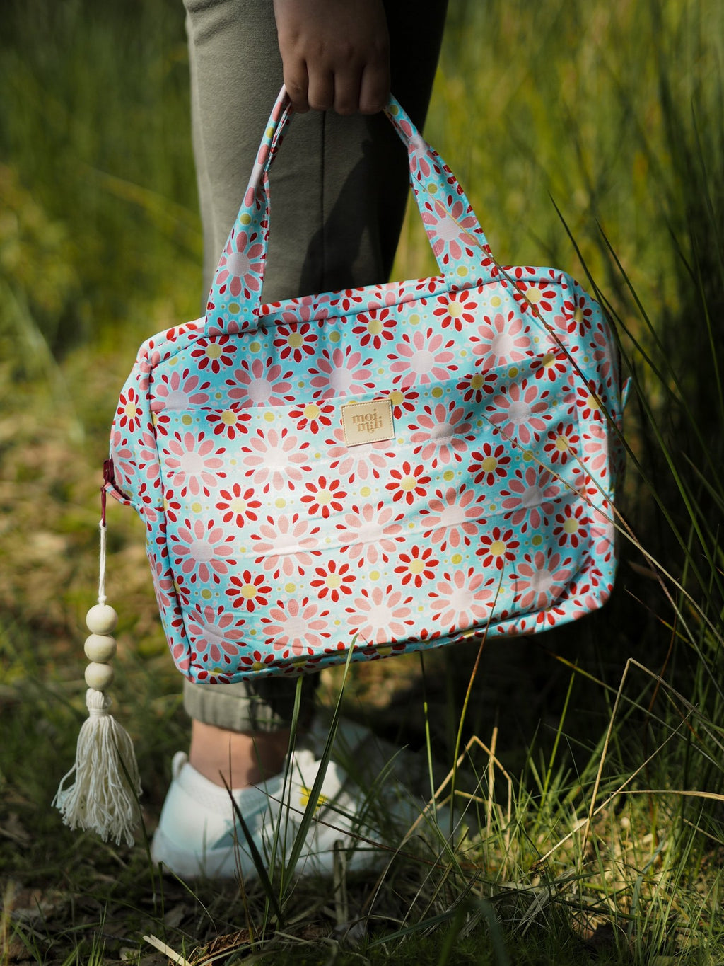 1. Person holding large floral makeup bag with tassel in outdoor setting