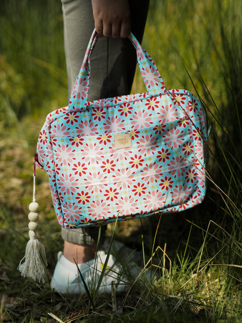 1. Person holding large floral makeup bag with tassel in outdoor setting