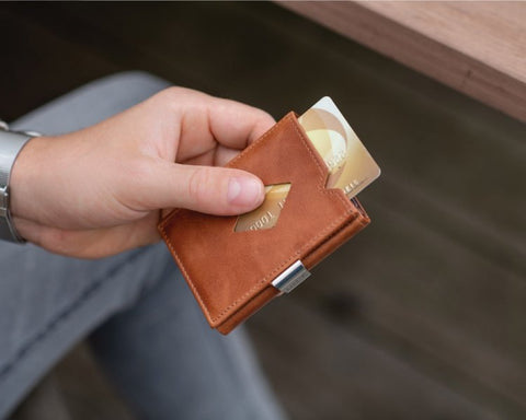 1. Person holding brown leather EXENTRI Multiwallet with visible credit cards outdoors