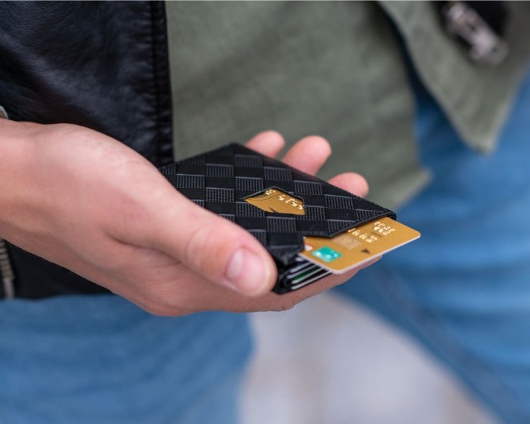 1. Person holding black EXENTRI wallet with chess pattern, showing card slots and thumb access feature