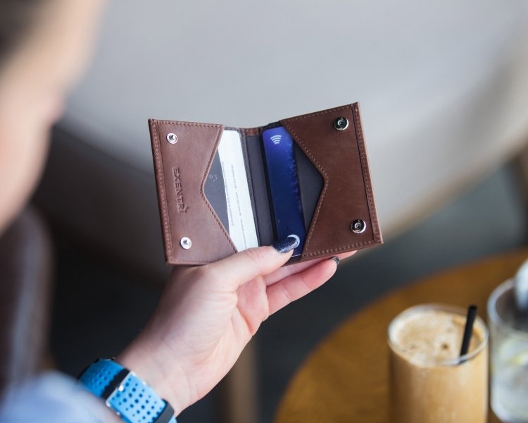 1. Person holding open brown EXENTRI Miniwallet showing card slots in a casual setting with a drink on the table