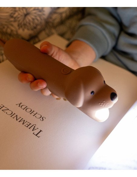 8. Child using brown dog-shaped silicone flashlight to read a book, emphasizing its functionality for bedtime storytelling.