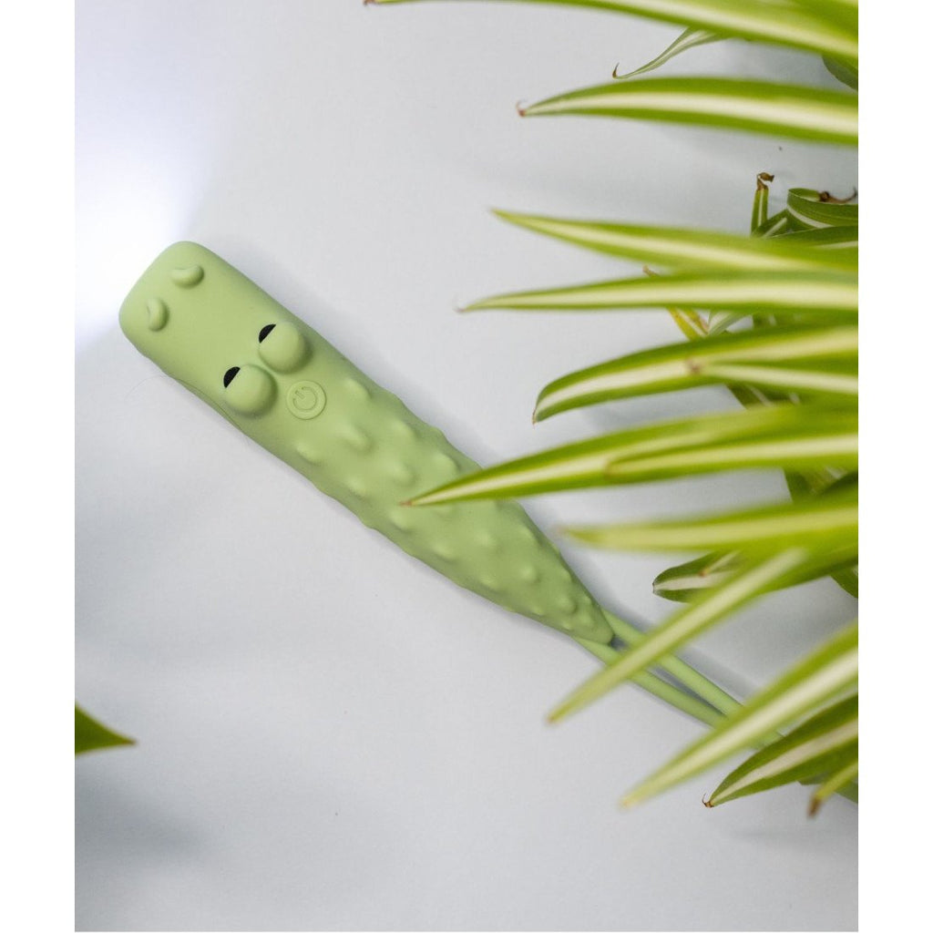 3. Green crocodile-shaped flashlight on white surface with plant leaves
