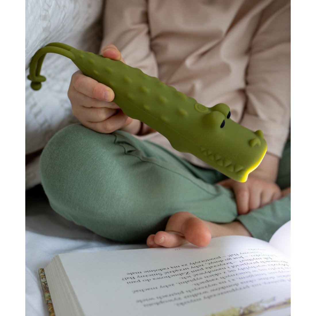 1. Child holding green crocodile-shaped flashlight while reading a book in bed