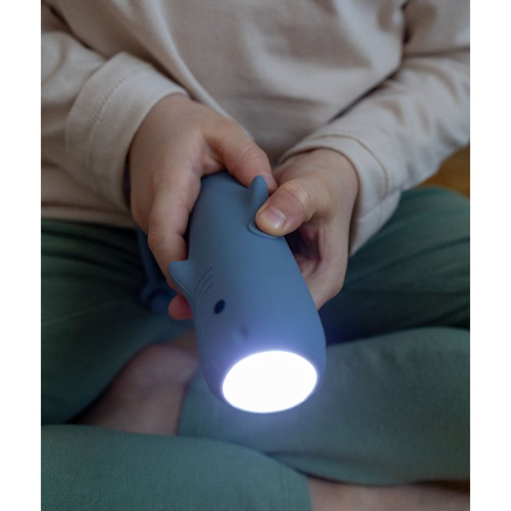1. Child holding blue shark-shaped flashlight with light on, sitting indoors