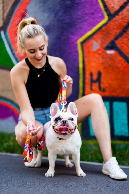 1. Woman smiling with a French Bulldog, holding a red graffiti dog leash against a colorful graffiti backdrop