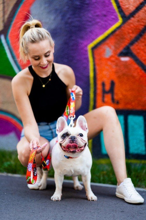 1. Woman smiling with a French Bulldog, holding a red graffiti dog leash against a colorful graffiti backdrop