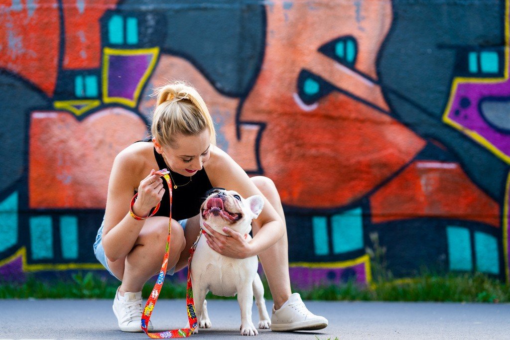 1. Woman crouching next to a French Bulldog, holding a red graffiti dog leash in front of a graffiti wall