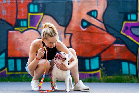 1. Woman crouching next to a French Bulldog, holding a red graffiti dog leash in front of a graffiti wall