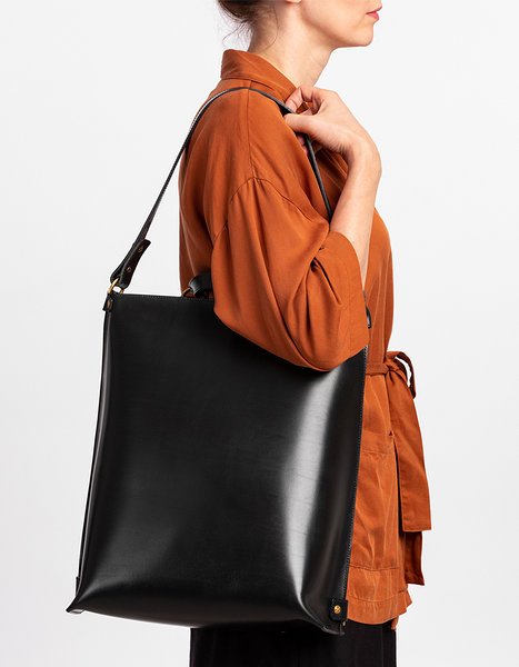 5. Woman holding black leather backpack by Stella Soomlais as shoulder bag, wearing orange shirt
