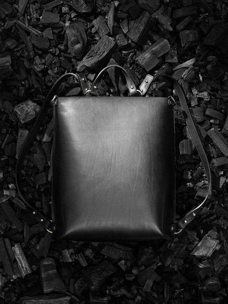 1. Black leather backpack by Stella Soomlais on textured dark background, showcasing sleek design and adjustable straps