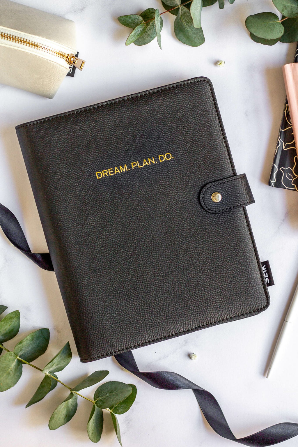 1. SEIK Premium Dream Plan Do Notebook with black vegan leather cover, featuring gold embossed text, surrounded by stationery and greenery