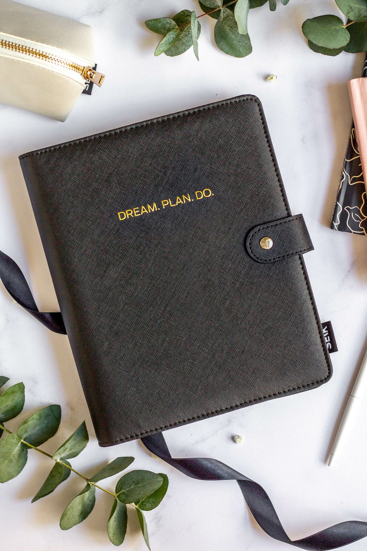 1. SEIK Premium Dream Plan Do Notebook with black vegan leather cover, featuring gold embossed text, surrounded by stationery and greenery