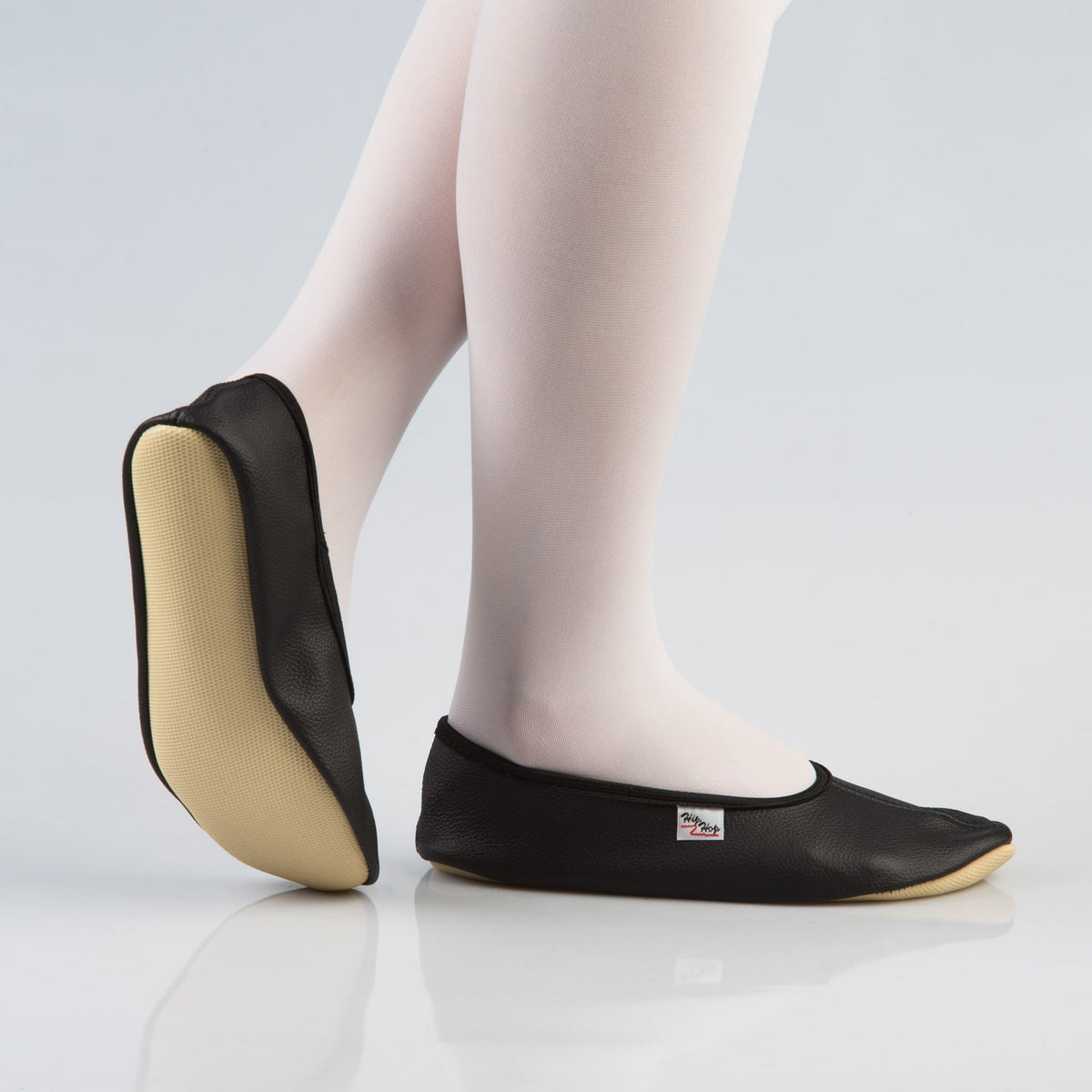 1. Women's black leather gymnastics slippers with rubber sole, shown in side view on model wearing white tights