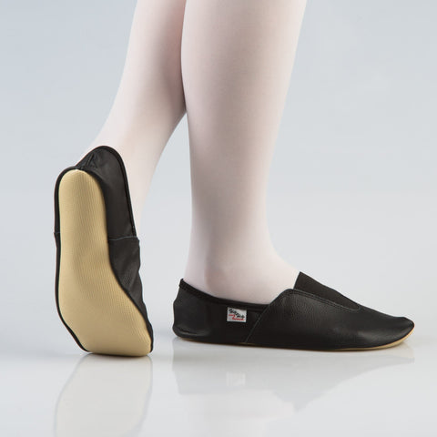 2. Side and sole view of women's black leather gymnastics slippers with rubber outsole, worn with white tights, studio setting