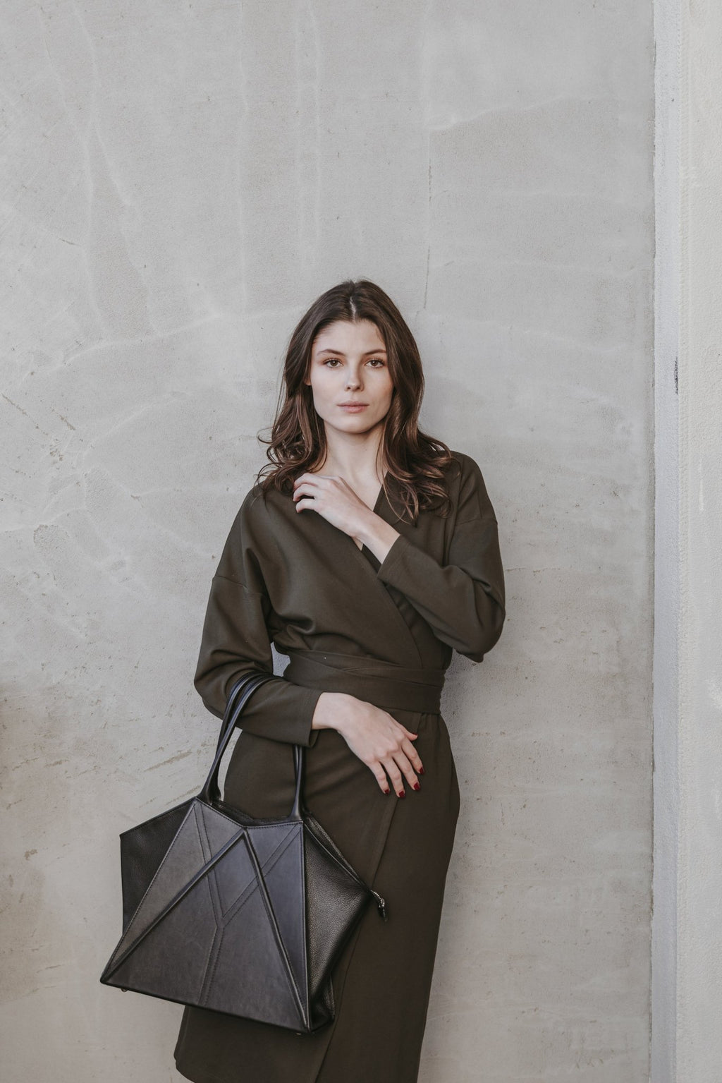 3. Woman posing with Gerda Retter Design Leather Handbag Nova in dark brown, seated in a stylish room with purple chairs