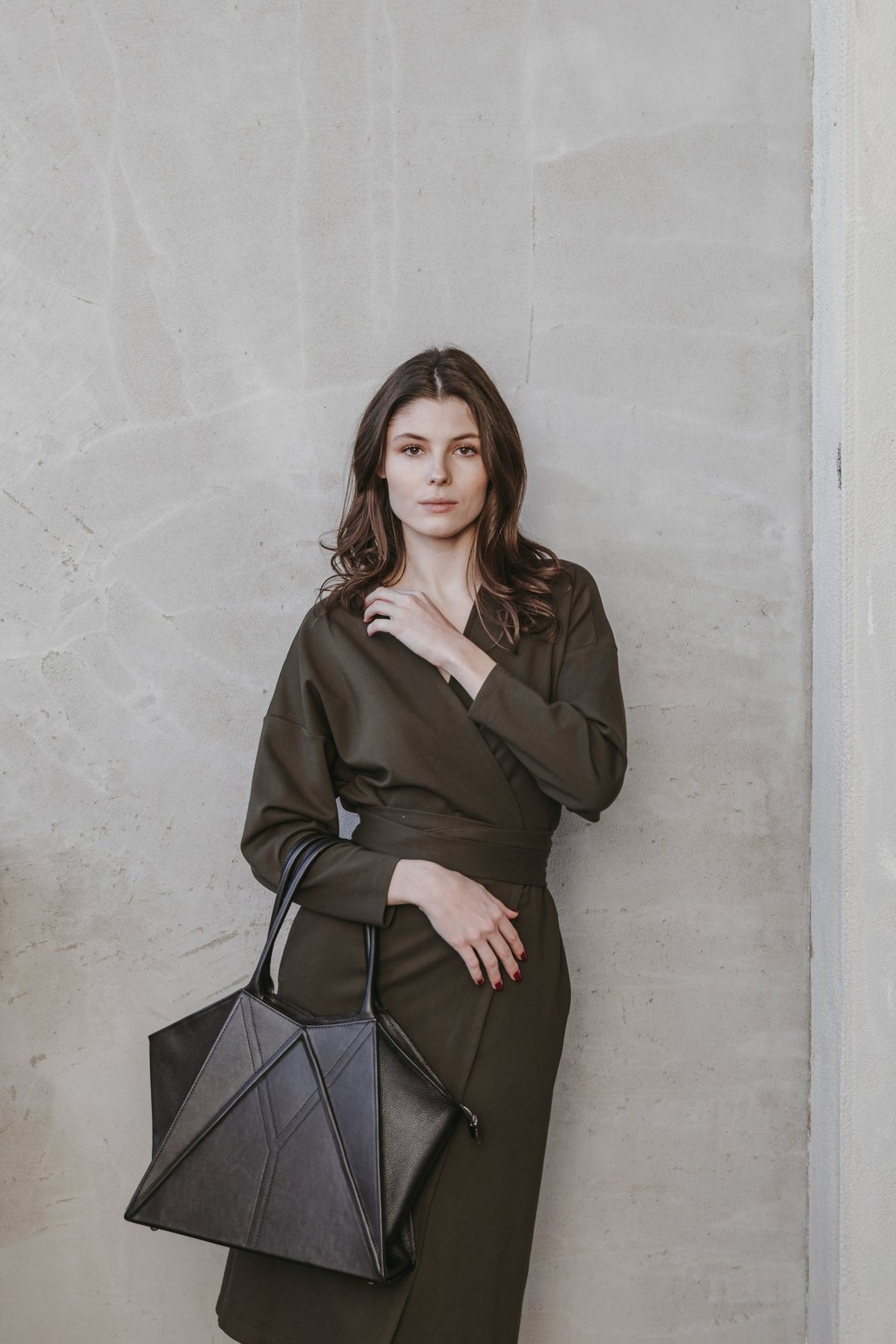 3. Woman posing with Gerda Retter Design Leather Handbag Nova in dark brown, seated in a stylish room with purple chairs