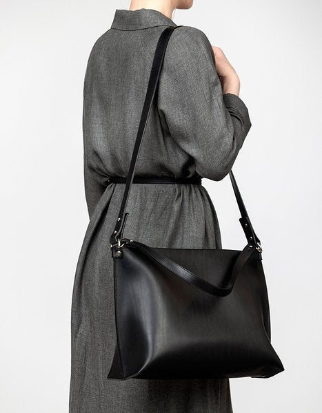 8. Woman in grey coat carrying Stella Soomlais black leather handbag, highlighting adjustable strap and minimalist design.