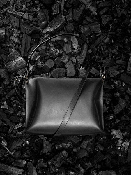 1. Black leather handbag by Stella Soomlais on a textured dark background, showcasing its sleek design and adjustable strap.