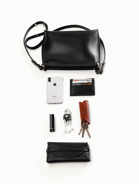 4. Flat lay of black leather Stella Soomlais handbag with essentials like phone, wallet, keys, and charger