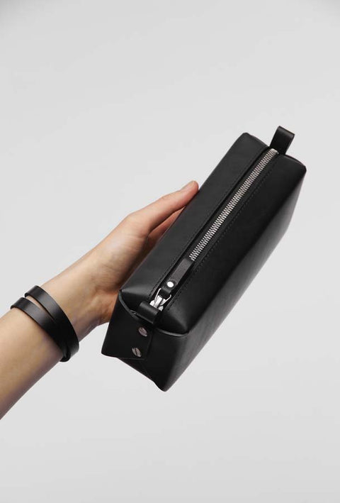1. Hand holding black leather makeup bag by Stella Soomlais with silver zipper, showcasing minimalist design