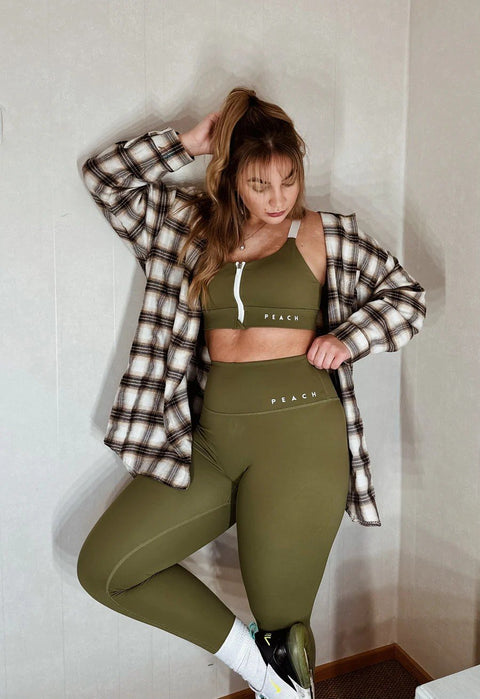 4. Woman in Peachlabel Olive Green leggings and plaid shirt indoors, demonstrating versatile styling