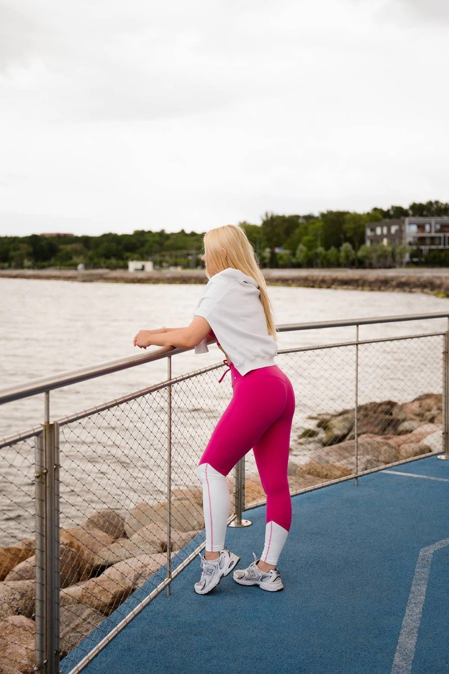 3. Back view of woman in Raspberry Dream leggings by Peachlabel, leaning on railing by the sea