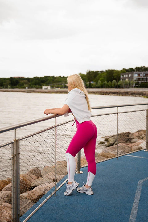 3. Back view of woman in Raspberry Dream leggings by Peachlabel, leaning on railing by the sea