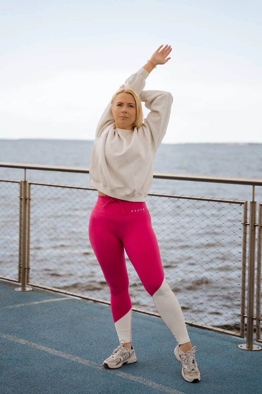 2. Woman stretching outdoors in Raspberry Dream leggings by Peachlabel, showcasing vibrant pink and white color block design