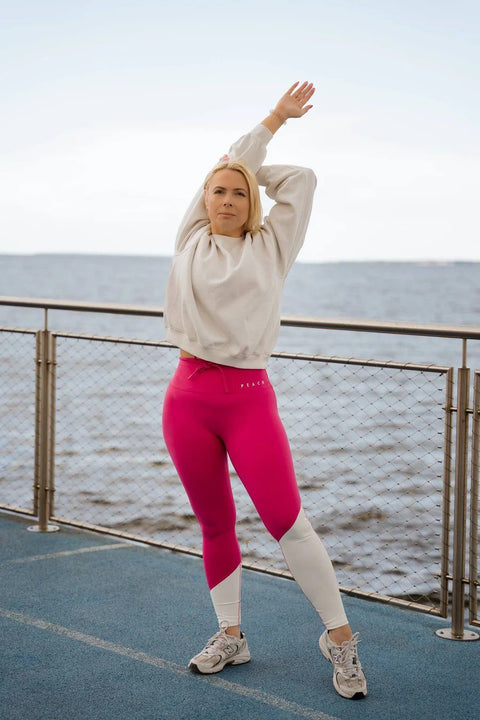 2. Woman stretching outdoors in Raspberry Dream leggings by Peachlabel, showcasing vibrant pink and white color block design