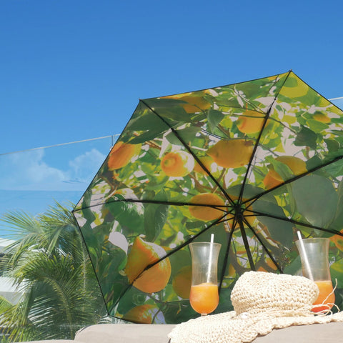 4. Lemon print umbrella open on sunny day with blue sky, accompanied by drinks and straw hat