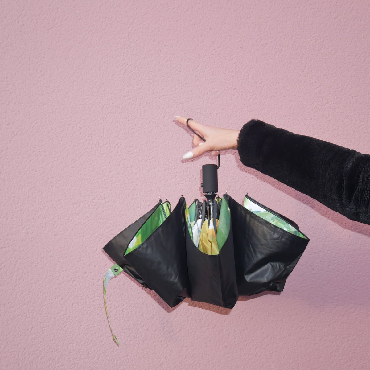 11. Hand holding partially open lemon umbrella with black exterior against pink wall
