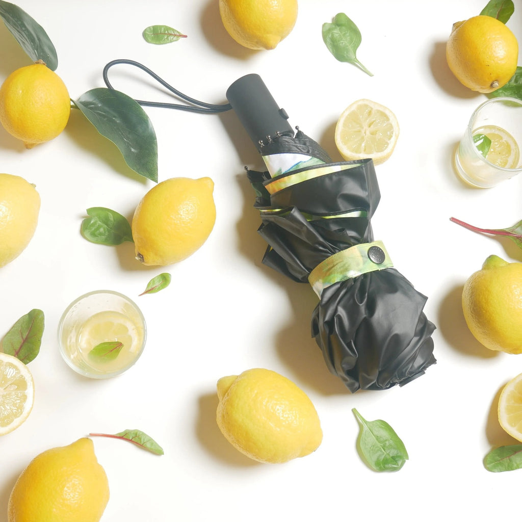 3. Compact lemon umbrella with black exterior surrounded by fresh lemons and leaves