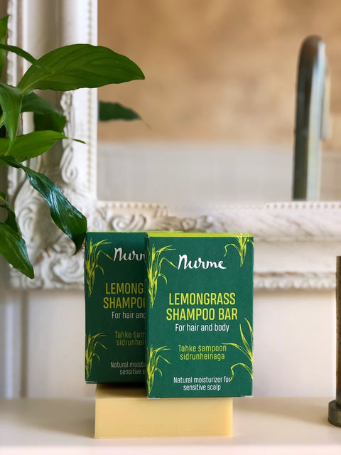 1. Two Nurme Lemongrass Shampoo Bars with green packaging on a bathroom counter with plant and mirror in background
