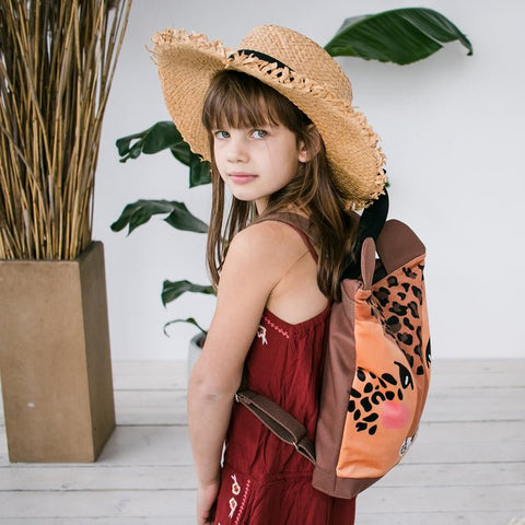 3. Girl wearing Muni leopard backpack, side view with straw hat in lifestyle setting