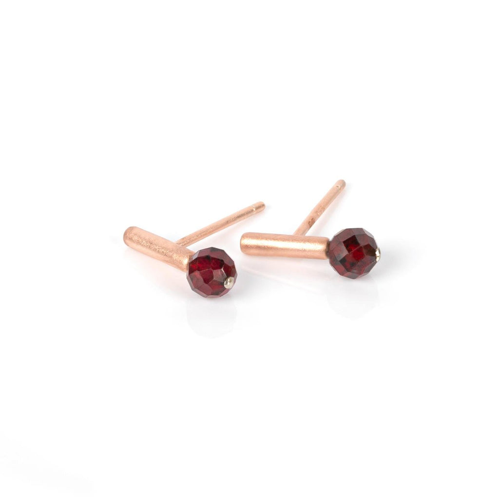 2. Pair of MyaMoon Light It Up earrings in rose gold with faceted red garnet stones on a white background