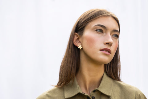 1. Woman wearing Lentsius Sunlit gold-tone flower earrings, gazing to the side with thoughtful expression