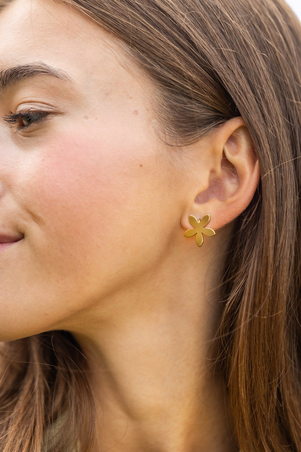 1. Woman wearing Lentsius Sunlit flower-shaped earrings in gold-tone, close-up of ear and cheek