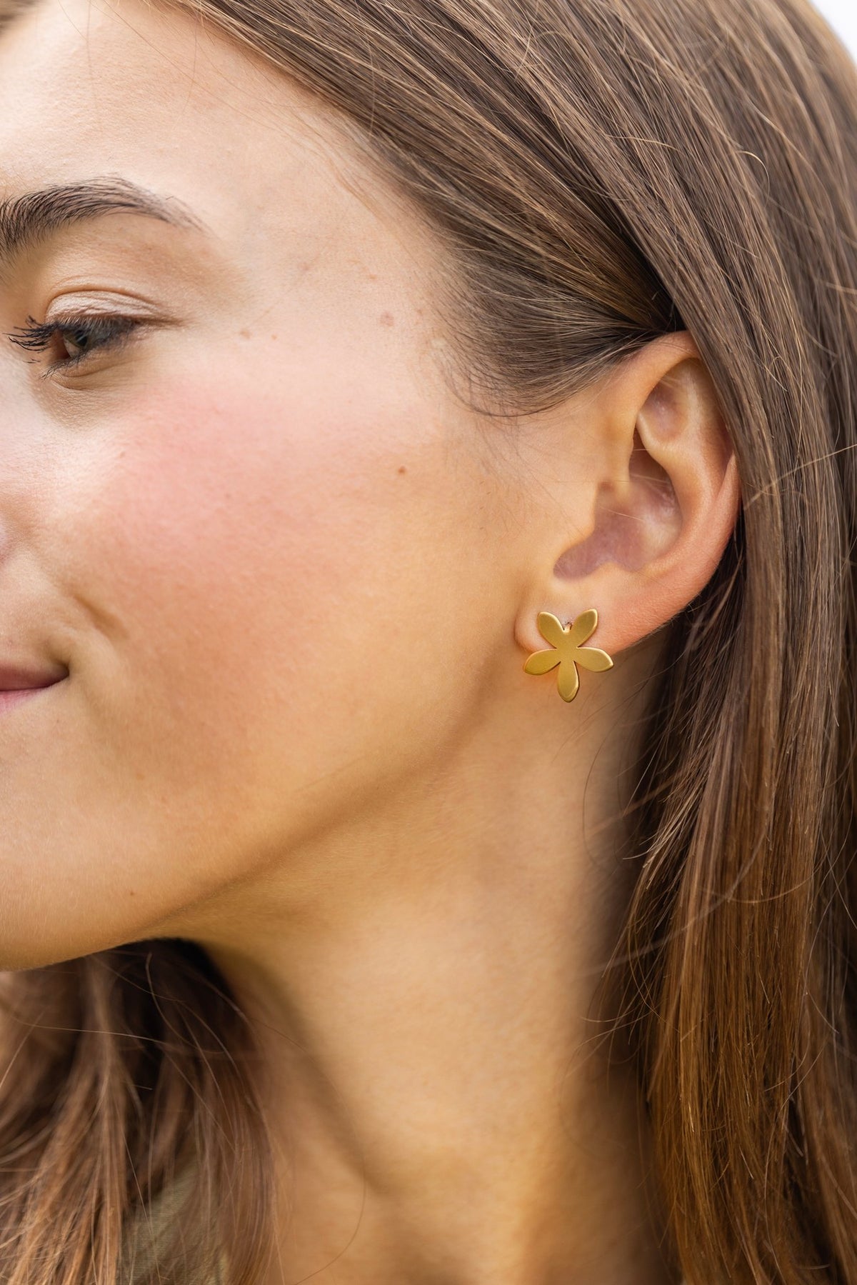 1. Woman wearing Lentsius Sunlit flower-shaped earrings in gold-tone, close-up of ear and cheek