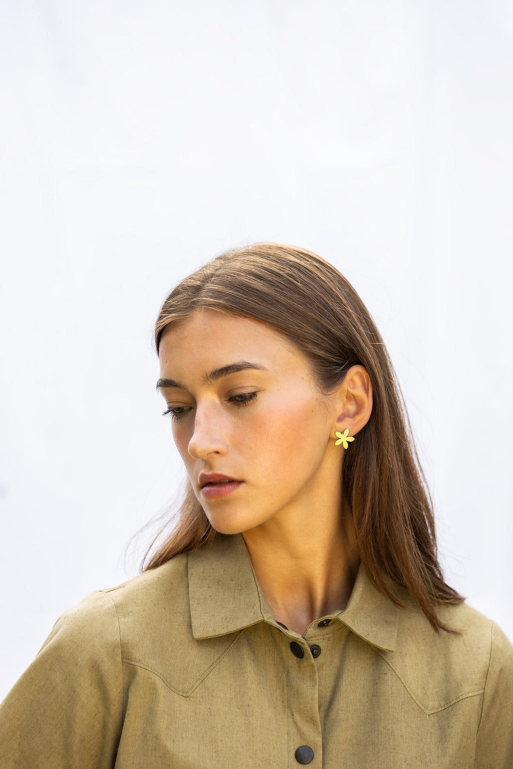 1. Woman wearing Lentsius Sunlit gold-tone flower earrings, looking down with contemplative expression