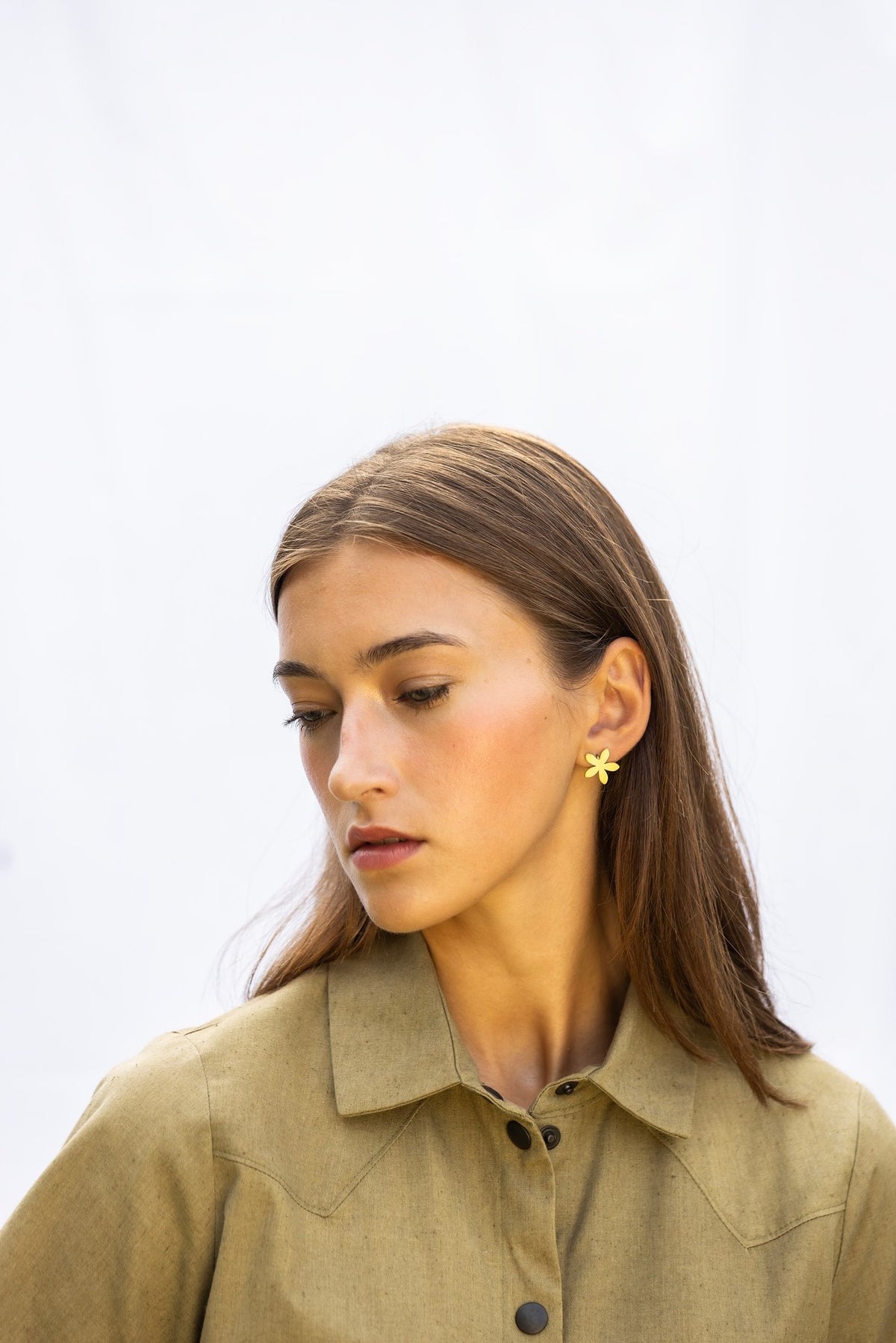 1. Woman wearing Lentsius Sunlit gold-tone flower earrings, looking down with contemplative expression