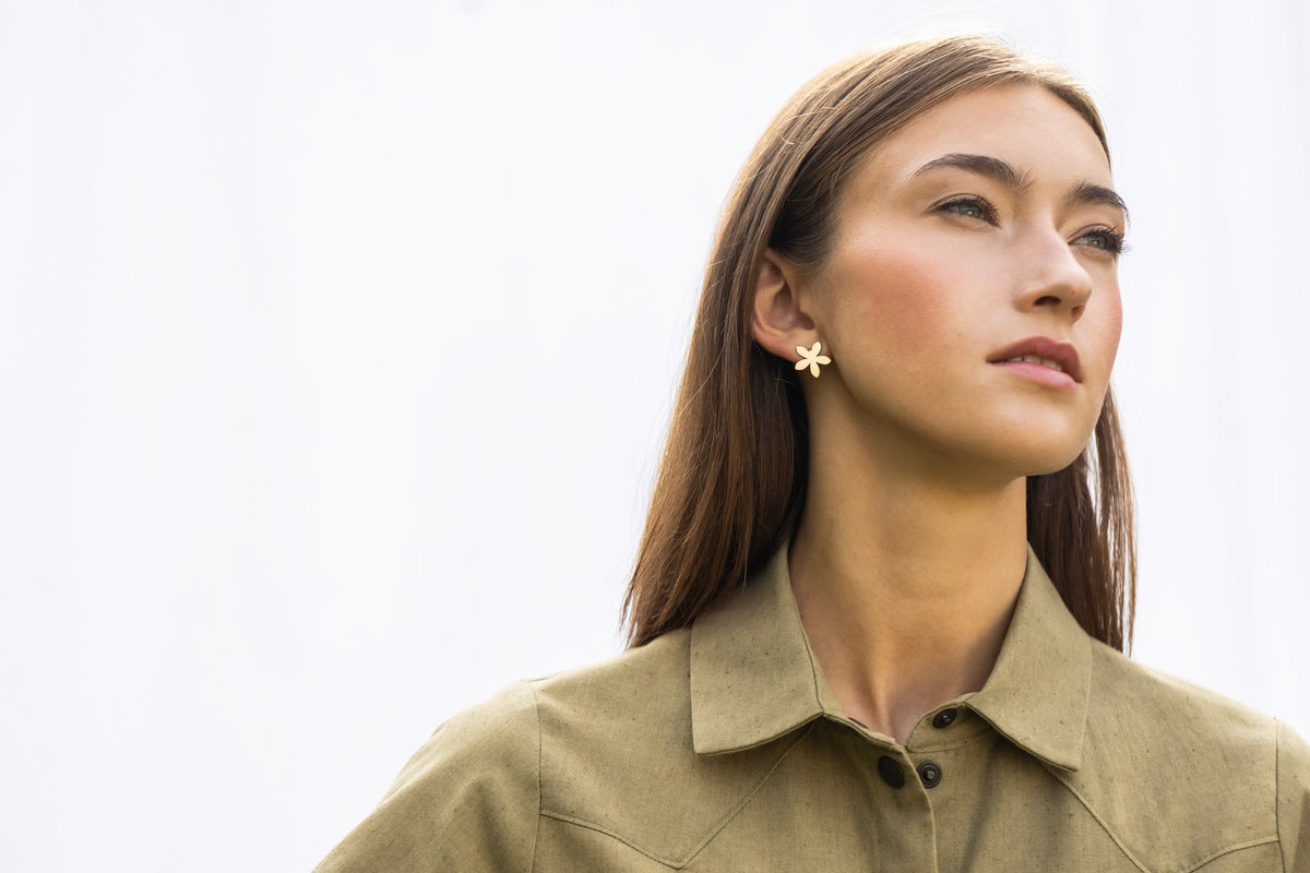 1. Woman wearing Lentsius Sunlit gold-tone flower earrings, looking into distance with serene expression