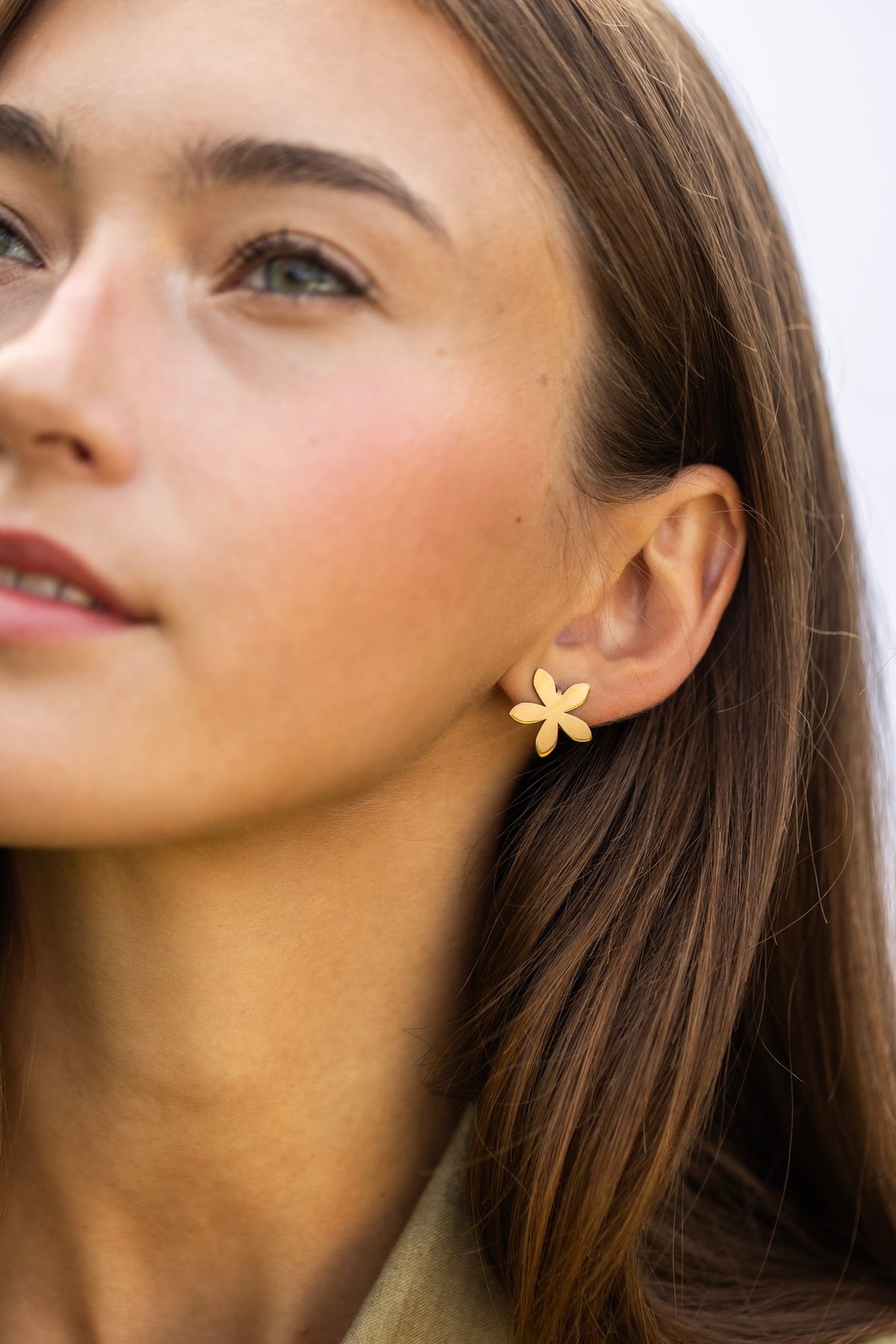 1. Woman wearing Lentsius Sunlit gold-tone flower earrings, looking upwards with soft expression